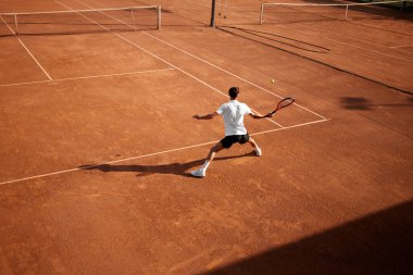 Dayanıklılık ve motivasyon. Odaklanmış adam, tenis oyuncusu kil sahada hareket halinde, topu alıyor, açık hava sahasında oynuyor. Spor anlayışı, rekabet, aktif ve sağlıklı yaşam tarzı