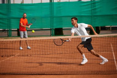 Yoğunlaşmış ve hırslı iki adam, açık hava kil kortunda tenis oyuncusu, odaklanmayla oynuyor, yoğunluğu ve oyunun ruhunu yakalıyor. Spor anlayışı, rekabet, aktif ve sağlıklı yaşam tarzı