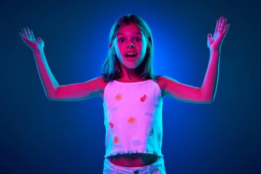 Sarı polo tişörtlü genç duygusal kızın portresi neon ışıkta mavi stüdyonun arka planına karşı şok, sürpriz ve heyecan ifade ediyor. Çocukluk kavramı, çocuk duyguları, yaşam tarzı