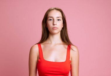 Güzel bir genç kadının portresi, kırmızı bluzlu öğrenci, pembe stüdyo arka planına karşı kendine güvenen bir şekilde poz veriyor. İnsan duyguları kavramı, yaşam tarzı, eğitim, haber
