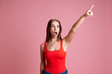 Kırmızı bluzlu duygusal genç bir kadının portresi. Şok olmuş ve heyecanlı bir yüzle poz veriyor. Pembe stüdyo arka planına doğru hareket ediyor. Haberler, satışlar, alışveriş. İnsan duyguları kavramı