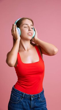 Güzel, genç, mutlu bir kızın portresi kulaklıkla müzik dinleyen pembe stüdyo arka planına karşı. Rahatlama ve meditasyon. İnsan duyguları kavramı, eğlence, eğlence, eğlence, eğlence