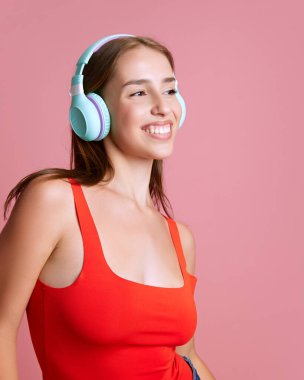 Güzel, genç, mutlu bir kızın portresi kulaklıkla müzik dinleyen pembe stüdyo arka planına karşı. İnsani duygular, eğlence, eğlence ve eğlence anlayışı.