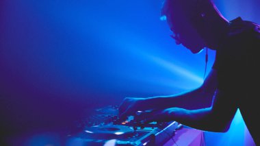 Işık ve ses senfonisi. DJ güverteye komuta ediyor, hareketleri dans pistini boyayan spot ışıklarıyla senkronize oluyor. Modern müzik ve teknoloji kavramı, parti, disko, gece hayatı.