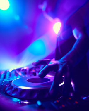 Neon ışıkların tayfıyla çevrelenmiş DJ, gece boyunca pürüzsüz akan parçaları harmanlıyor ve titreşimi kontrol ederken dikkati hiç dağılmıyor. Modern müzik ve teknoloji kavramı, parti, disko, gece hayatı.
