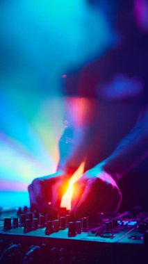 DJ, dönen ışıklarla çevrili, hipnotik seti karıştırıyor, vücudu neredeyse havayı dolduran canlı renklerle birleşiyor. Modern müzik ve teknoloji kavramı, parti, disko, gece hayatı.
