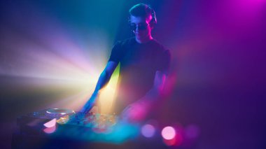 Kulaklıklar içindeki DJ, canlı ışıklara daldı, renkler etrafında dolaşırken ritmleri karıştırdı, heyecan verici bir atmosfer yarattı. Modern müzik ve teknoloji kavramı, parti, disko, gece hayatı.