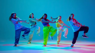 Spor tarzı giyinmiş beş genç kızın dinamik görüntüsü neon arka planda Cyan mavisi arka planda hip hop dansı yapıyor. Sokak tarzı. Modern dans stilleri, gençlik kültürü, aktif yaşam tarzı kavramı