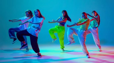 Bir grup genç dansçı, dinamik hareketler yapan kızlar, neon arka planda cyan mavisi arka planda hip hop dansı yapan kızlar. Modern dans stilleri, gençlik kültürü, aktif yaşam tarzı kavramı