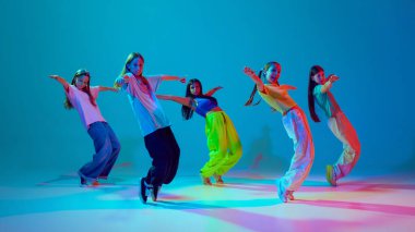 Genç kızların dinamik senkronize hareketleri, hareketli gençler, neon arka planda cyan mavisi arka planda hip hop dansı. Modern dans stilleri, gençlik kültürü, aktif yaşam tarzı kavramı