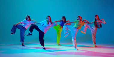 Ritim ve enerji. Bir grup çocuk, hip hop yetenekleri sergileyen kızlar, neon arka planda siyan mavisi arka planda dans ediyorlar. Modern dans stilleri, gençlik kültürü, aktif yaşam tarzı kavramı