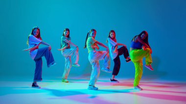 Spor tarzında giyinmiş genç kızların neon arka planda Cyan mavisi arka planda hip hop yaparken dinamik görüntüsü. Modern dans stilleri, gençlik kültürü, aktif yaşam tarzı kavramı