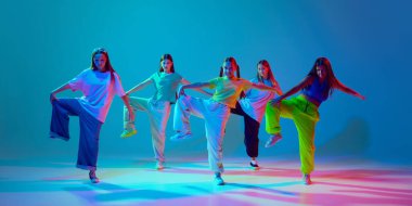 Spor tarzında giyinmiş genç kızların neon arka planda Cyan mavisi arka planda hip hop yaparken dinamik görüntüsü. Modern dans stilleri, gençlik kültürü, aktif yaşam tarzı kavramı