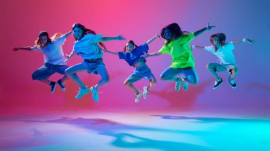 Ateşli hip hop pozları veren genç kızlar, neon ışıklarıyla değişken pembe arka plana karşı enerjik bir şekilde dans ediyorlar. Modern dans stilleri, gençlik kültürü, aktif yaşam tarzı kavramı