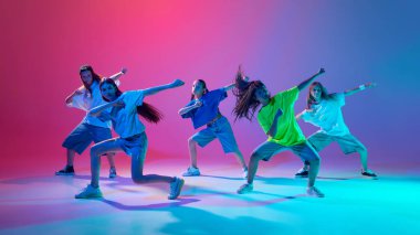 Genç dansçılardan oluşan dinamik bir grup, neon ışıkta değişken pembe arka plana karşı enerjik hip hop performansı sergileyen genç kızlar. Modern dans stilleri, gençlik kültürü, aktif yaşam tarzı kavramı
