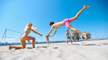 Dinamik oyun. Pozitif ve aktif gençler, sahilde toplanan arkadaşlar ve enerjik frizbi oyunu. Spor anlayışı, yaz etkinliği, eğlence oyunları, arkadaşlık.