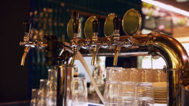 Yumuşak bar ışıkları altında ön planda boş bardaklarla koyu arka planda parlayan klasik bira muslukları. Bira, bira fabrikası, bar, Ekim Festivali, gelenekler