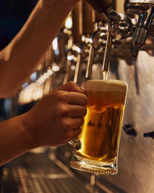 Kadın barmen fıçıdan köpüklü birayı bardağa dolduruyor. Modern bira barı, restoran. Bira, bira fabrikası, bar, Ekim Festivali, gelenekler