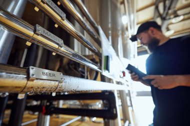 Teknoloji uzmanı bira sistemini yakından inceleyerek etiketlenmiş her borunun üretim planıyla aynı hizaya geldiğini doğruladı ve demleme süreci üzerinde katı bir kontrol sağladı. Bira, bira fabrikası, kalite kontrol kavramı