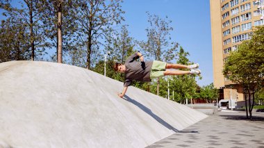 Yer çekimine meydan okuyan genç atletik bir adam bir elinde yanlamasına denge kurarak parkour için beton yamaca karşı gereken gücü gösteriyor. Aktif ve sağlıklı yaşam tarzı kavramı, gençlik kültürü
