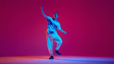 Genç bir adamın dinamik görüntüsü, sokak tarzı kıyafetlerle dans eden ve eflatun bir stüdyoda hip-hop yapan bir dansçı. Hobi, eğlence, performans, yaratıcılık kavramı