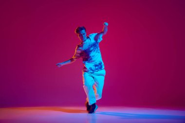 Genç bir adamın dinamik görüntüsü, sokak tarzı kıyafetlerle dans eden ve eflatun bir stüdyoda hip-hop yapan bir dansçı. Hobi, eğlence, performans, yaratıcılık kavramı
