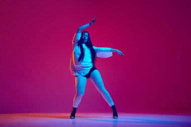 Hip-hop ve yüksek topuklu dansların karışımı. Güzel genç bir kadın dans ediyor, eflatun renkli stüdyo geçmişine karşı yaratıcı bir performans sergiliyor. Hobi, eğlence, performans, yaratıcılık, yaşam tarzı kavramı