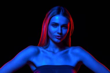 Kusursuz cilt ve düz saçlarla siyah stüdyo arka planında neon ışıkta duran güzel genç bir kadının portresi. Doğal güzellik kavramı, cilt bakımı, kozmetik, sağlık, kaplıca.