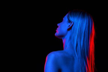 Mükemmel uzun saçlı ve çıplak omuzlu bir kadın neon ışıkta siyah stüdyo arka planına karşı. Özel bakım ve kozmetik ürünleri. Arkadan bak. Doğal güzellik kavramı, cilt bakımı, kozmetik, sağlık, kaplıca.