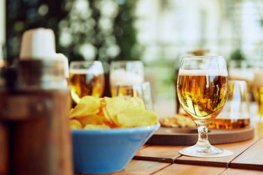 Güneşli bir günde, açık kafedeki ahşap masada bir kase bira ve patates cipsi. Parti anlayışı, kutlama, eğlence zamanı, Ekim Festivali