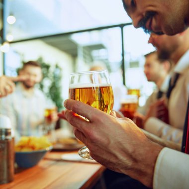 Bira tutan erkek eline odaklan. İş adamları, iş arkadaşları yerel barda buluşuyor, bira içiyor, konuşuyor ve başarılı işbirliğini kutluyorlar. İş anlayışı, toplantı, eğlence, Ekim Festivali