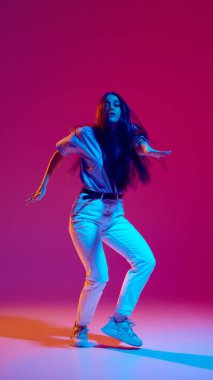 Ritmi yakalıyorum. Genç enerjik bir kadın günlük giysiler içinde dinamik hareketler yapıyor, neonlu eflatun arka planda hip-hop dansı yapıyor. Sokak tarzı kavramı, modern dans, eğlence
