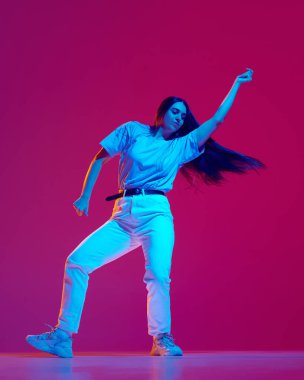 Genç, yetenekli ve sanatsal bir kadının enerjik bir hip-hop performansı ile neonlu pembe arka plan, tam boy dinamik görüntüsü. Sokak tarzı kavramı, modern dans, eğlence