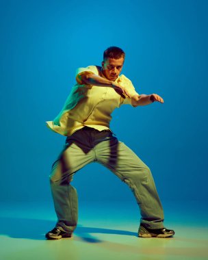 Yetenekli, sanatsal, gündelik kıyafetlerle dans eden, neon rengi mavi arka planda tutku ve becerilerle hip-hop yapan enerjik bir genç. Sokak tarzı kavramı, modern dans, eğlence