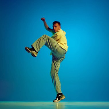 Hip-hop enerjisi. Sanatçı ve yaratıcı genç bir adam, neon ışıkta mavi arka plana karşı tutkuyla dans eden bir dansçı. Sokak tarzı kavramı, modern dans, eğlence