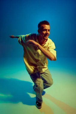 Şehir ritmi ve akışı. Gündelik kıyafetlerle dans eden yetenekli genç bir adamın dinamik görüntüsü neon ışıkta, değişken mavi arka planda hip-hop yapıyor. Sokak tarzı kavramı, modern dans, eğlence