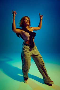 Tutkulu ve sanatsal dansçı, şık gündelik kıyafetler giymiş enerjik bir performans sergiliyor, mavi arka planda hip-hop dansı yapıyor. Sokak tarzı kavramı, modern dans