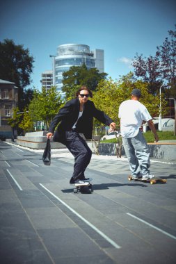 Sokak ve klasik tarzın karışımı. Kamu parkında hareket halindeki iki adam, şehir binalarının arka planında kaykay yapıyor. Spor anlayışı, aktivite ve hareketler, hobi