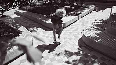 Gündüz vakti halka açık yerlerde tutkuyla kaykay yaparken enerji ve özgürlüğünü ifade eden günlük giysiler içindeki kıvırcık genç adam. Siyah beyaz fotoğrafçılık. Spor, aktivite ve hareket kavramı