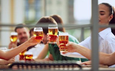 Şehir barının terasında oturan ve bira bardaklarını tokuşturan gençler uzun yıllar sonra buluşmayı kutluyorlar. Seçici odaklanma. Cuma havası, kutlama, öğle tatili ve Ekim Festivali kavramı.