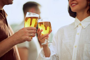 İki bardak bira neşeli bir tostun içinde buluşur, dostluğun ve güzel zamanların özünü yakalar. Güneş ışığı altın sıvıya yansıyarak anı güçlendirir. Cuma havası, kutlama, Ekim Festivali kavramı.