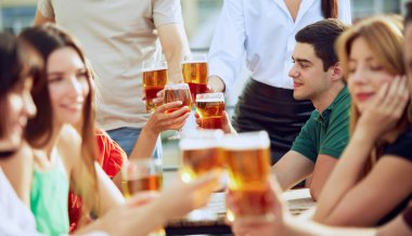 Neşeli grup terasta soğuk biraları, kadeh tokuşturmayı ve gülümsemeyi, arkadaşlığı ve hayatın basit zevklerini kutlamayı sever. Cuma havası, kutlama, öğle tatili ve Ekim Festivali kavramı.