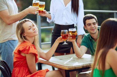 Neşeli grup terasta soğuk biraları, kadeh tokuşturmayı ve gülümsemeyi, arkadaşlığı ve hayatın basit zevklerini kutlamayı sever. Cuma havası, kutlama, öğle tatili ve Ekim Festivali kavramı.