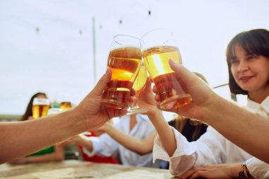 Arkadaşlar masanın etrafında toplanır, kadehlerini güzel zamanlara kaldırırlar. Canlı atmosfer ve paylaşılan kahkahalar güneşli bir günü mükemmel kılıyor. Cuma havası, kutlama, Ekim Festivali kavramı.