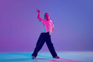 Şık giyinmiş, tutkulu ve enerjik genç bir kız neon ışıkta değişen mor arka plana karşı hip hop yapıyor. Serbest stil dansı, modernlik, şehir kültürü, gençlik kavramı