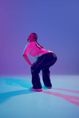 Ritmi yakalamak. Şık ve sanatsal genç kız, hip-hop dansçısı, neon ışıkta mor arka plana karşı tutkuyla sahnede performans sergiliyor. Serbest dans kavramı, şehir kültürü, gençlik