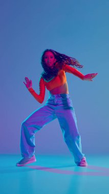 Enerji patlaması. Hareketli genç bir kız, neon ışıkta, değişken mavi arka planda, dinamik olarak hip hop yapıyor. Serbest stil dansı, modernlik, şehir kültürü, gençlik kavramı