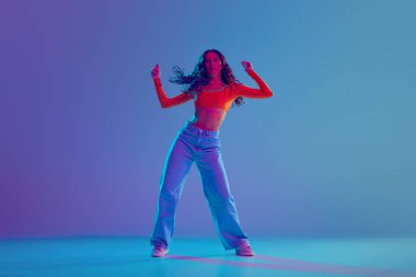 Dansçı kadın, performans sırasında neon ışıkta değişken mavi arkaplan karşısında akışkan hip hop hareketlerini sergiliyor. Serbest stil dansı, modernlik, şehir kültürü, gençlik kavramı