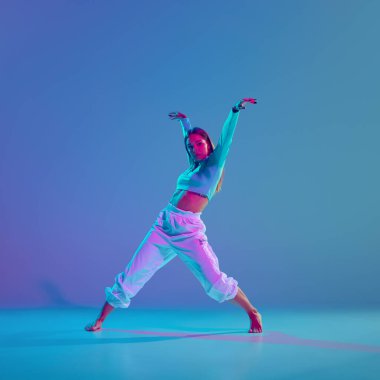 Gençlik enerjisi, dinamik hip hop koreografisi. Genç, yetenekli ve sanatsal kız, neon ışıkta, gradyan mavi arka planda performans sergiliyor. Serbest stil dansı, modernlik, şehir kültürü, gençlik kavramı