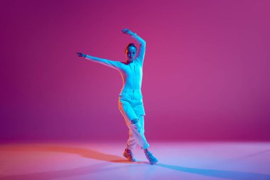 Beyaz kıyafetli, yetenekli ve sanatsal genç kız neon ışıkta pembe arka planda hip-hop dansı yapıyor. Serbest stil dansı, modernlik, şehir kültürü, gençlik kavramı